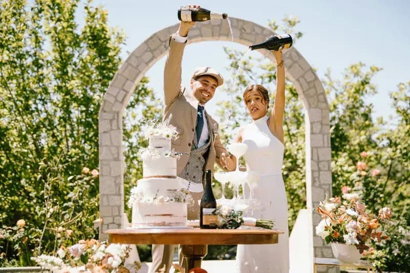 Bride and groom pouring champagne into a glass tower at an outdoor wedding